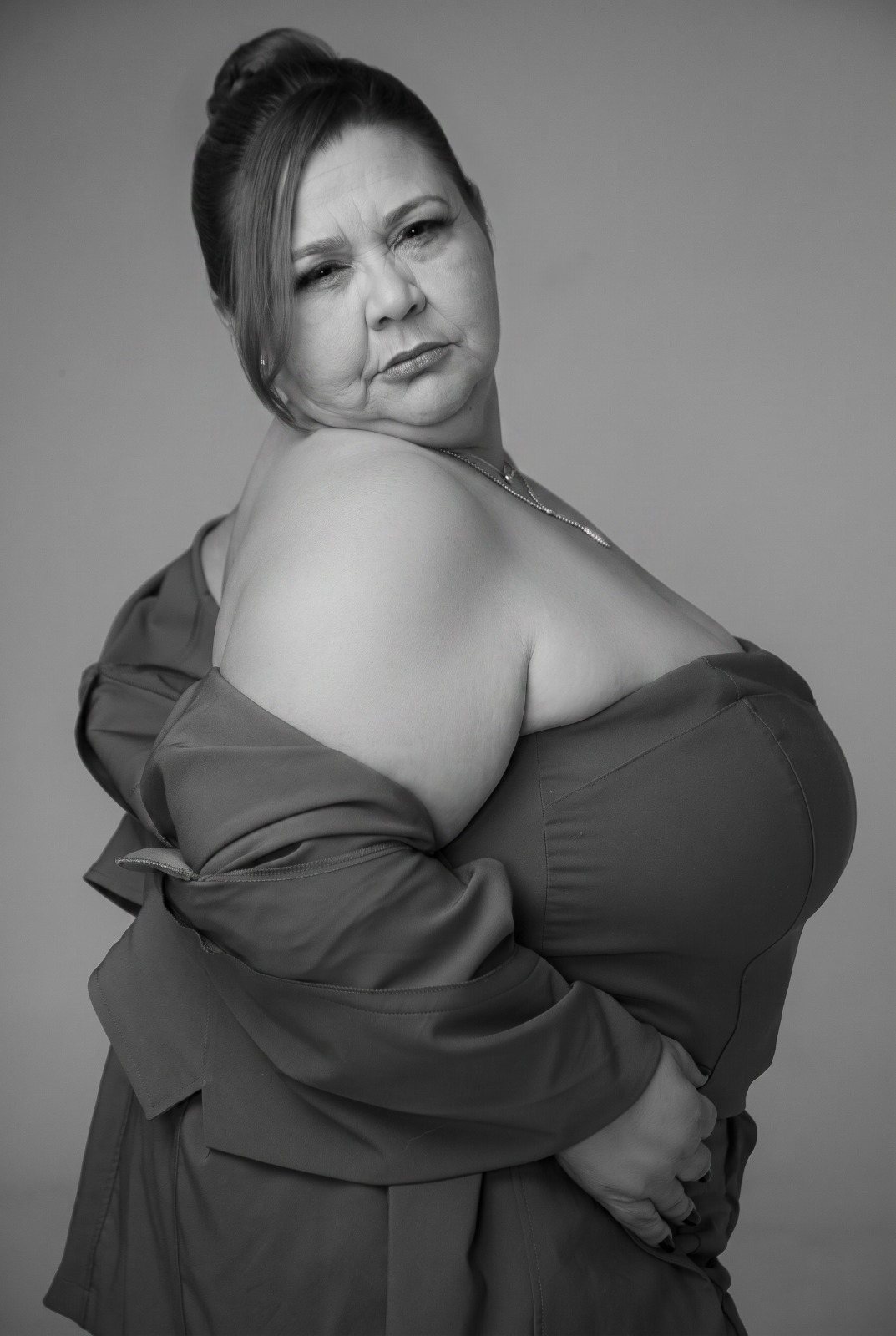 Retrato de estúdio em preto e branco de mulher plus size de vestido, postura ereta, olhar confiante, sem câmeras ao redor.